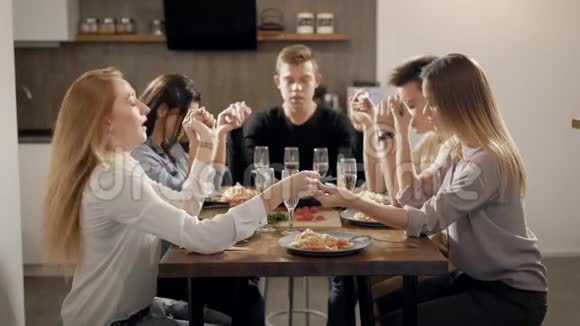 一大群亲密的朋友坐在餐桌旁手牵着手在晚餐前祈祷视频的预览图