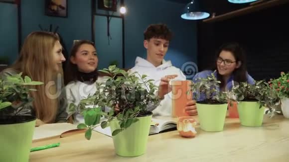 四个年轻的学生坐在咖啡馆里课间休息笑着开玩笑吃零食喝咖啡视频的预览图