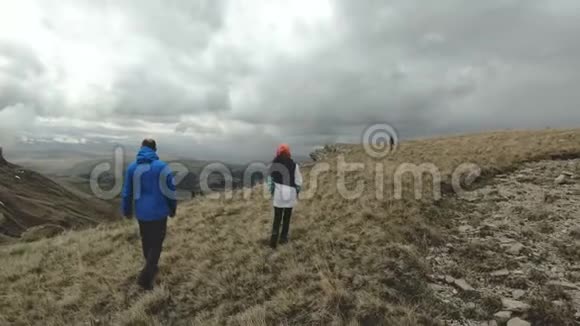 一群游客三人在多云的天气下行走在高原边缘的高山上慢动作视频的预览图