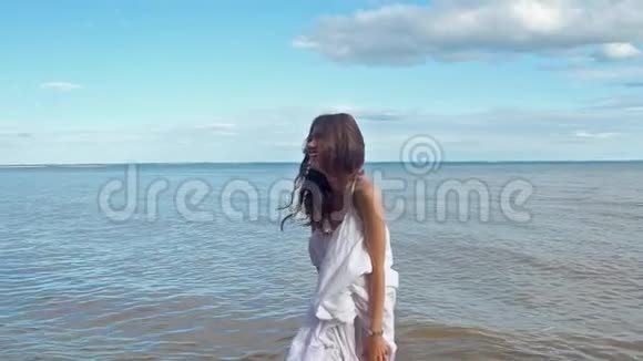 美丽的女孩穿着白色的夏装在蓝色的海洋背景上笑得很开心视频的预览图