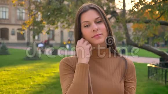 在绿色公园背景下美丽的黑发美女戴上耳机随着音乐跳舞的肖像视频的预览图
