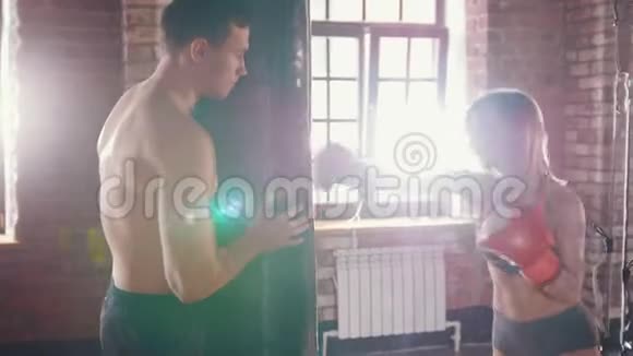 健身房里的男人和女人教练拿着一个拳击袋女人打了它一个太阳从窗户出来视频的预览图