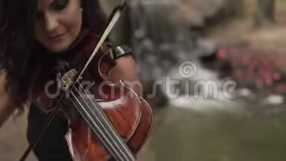 在森林里用瀑布拉小提琴的美丽少女视频的预览图
