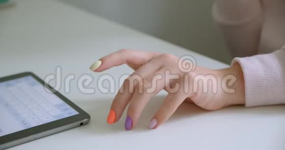 女性手的特写镜头使用平板电脑进行漂亮的指甲修剪并敲击桌子等待室内视频的预览图