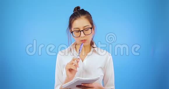 那个女孩在笔记本上写笔记蓝色背景眼镜学生视频的预览图