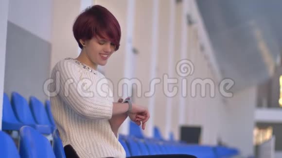快乐美丽的粉红头发女孩坐在体育场看手表的肖像视频的预览图