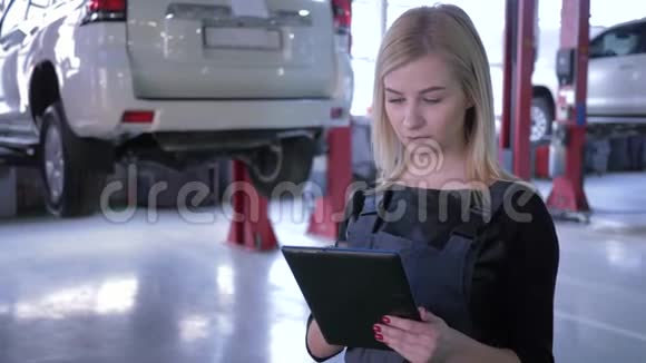 专业的女机械师在一家汽车修理厂使用平板电脑背景是液压升降机上的汽车视频的预览图