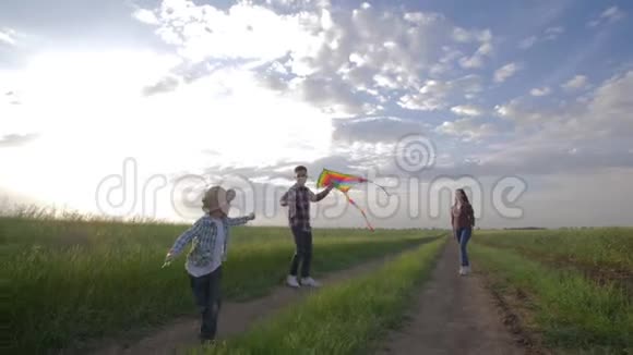 家庭放风筝男孩带着年轻的父母周末在农村以大自然的天空为背景奔跑视频的预览图