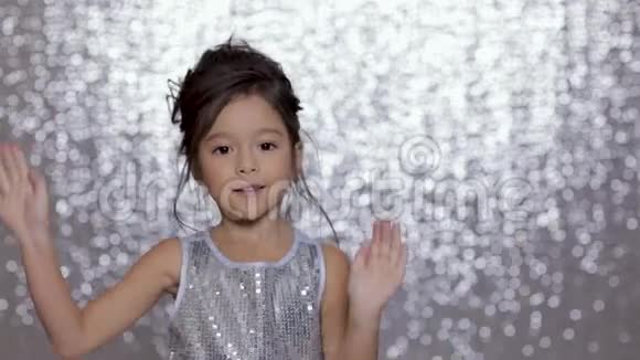 可爱快乐的小女孩穿着银色的裙子在银色的背景下跳舞视频的预览图