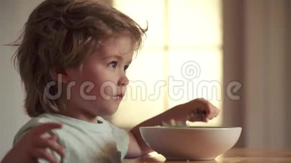 年轻的孩子坐在桌子上吃健康的食物脸上有滑稽的表情孩子吃东西嘲笑可爱的孩子宝宝视频的预览图