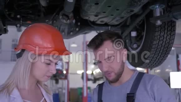 女客户戴安全帽汽车修理工在维修服务站检查汽车视频的预览图