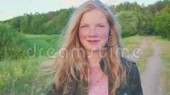 一个十几岁的女孩走在森林附近的田野上享受着大自然的夜晚这孩子有一头金发她是视频的预览图