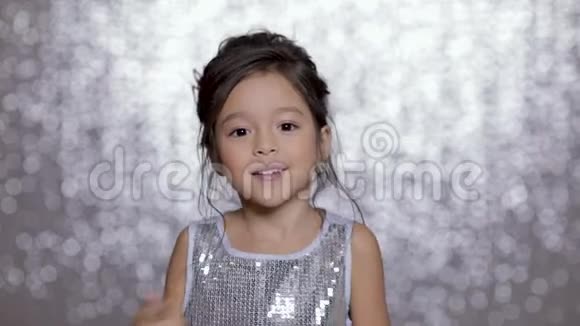 美丽的微笑的小女孩穿着银色的裙子在银色的背景下跳舞视频的预览图