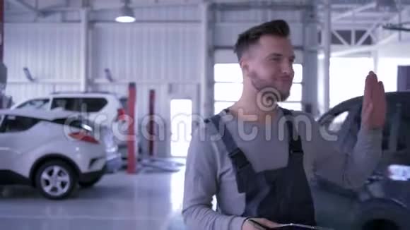 微笑的机械师走在服务站手挥向过往的汽车手拿着剪贴板的迷人男子视频的预览图
