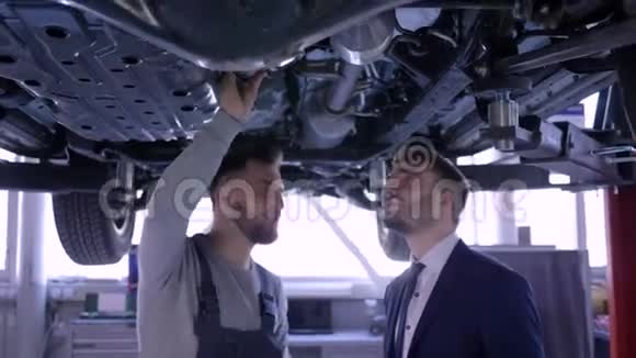 汽车机械师检查技术状况汽车机械升降机与客户服务然后快乐的男人摇动视频的预览图