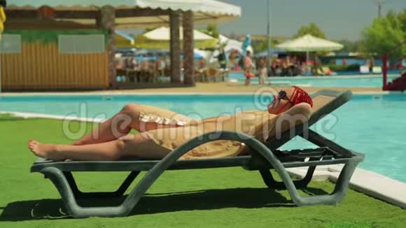一位穿着浴袍的年轻女子在游泳池附近的一张躺椅上晒太阳视频的预览图