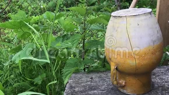 旧的开裂陶瓷水壶仰面向下站在腐朽的木架上杂草丛中视频的预览图