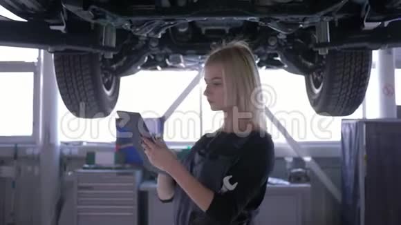 女汽车修理工在维修服务站用背光板检查举升的汽车视频的预览图
