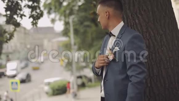 英俊的新郎待在城市街道的树旁婚礼那天慢动作很少有镜头视频的预览图