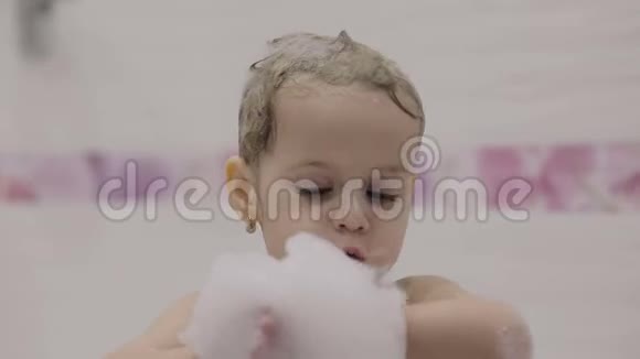 漂亮的三岁女孩洗澡用沐浴泡沫弄湿头发可爱的金发孩子手里拿着泡沫然后吹视频的预览图