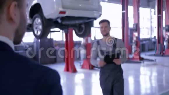 汽车服务机械师向他的客户解释汽车修理费用写在剪贴板上握手视频的预览图