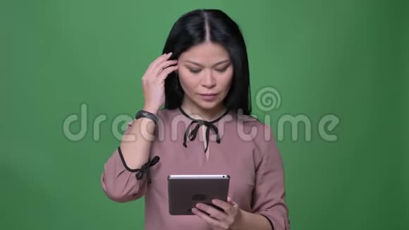 年轻迷人的黑发亚洲女性的特写镜头使用的平板电脑背景隔离在绿色视频的预览图