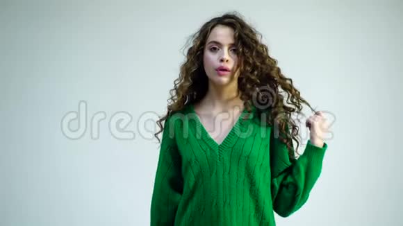 穿绿色毛衣的时尚女性快乐美丽的卷发女孩牙齿上戴着牙套手指上裹着头发视频的预览图