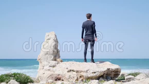 站在海滩大岩石上的年轻白种人戴上太阳镜开始奔跑视频的预览图