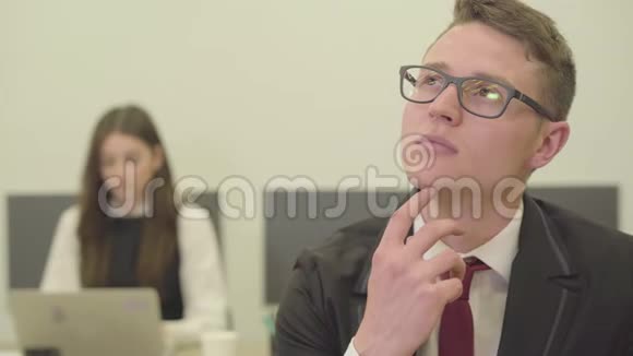 一幅有思想的年轻男子戴着眼镜坐在办公室的前台而他的女同事则在正式场合视频的预览图
