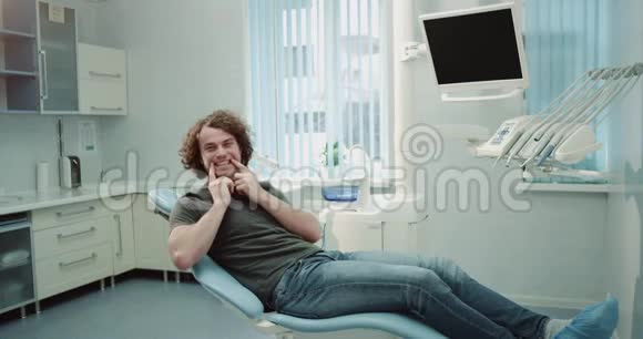 有魅力的年轻病人在牙科诊所等待他的牙医并在镜头前展示他完美的白色视频的预览图