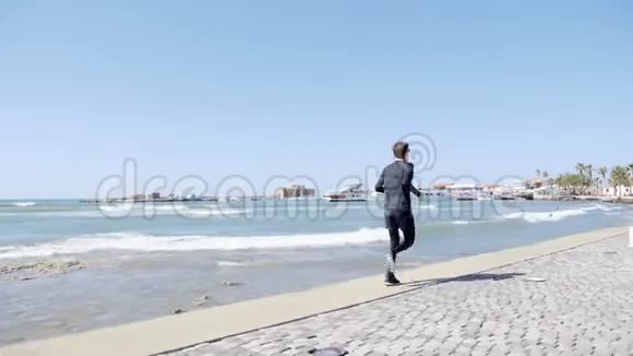 一个年轻迷人的白种人穿着黑色衣服在码头上跑步背射视频的预览图