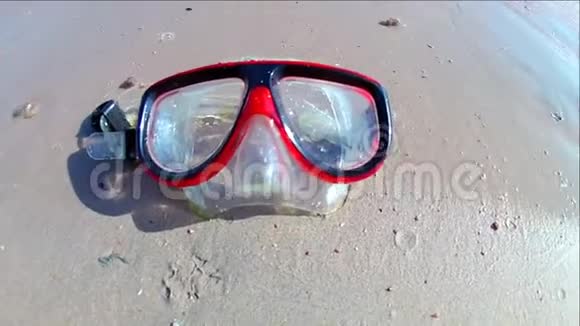 一个潜水面具躺在沙质的海岸上海浪在阳光明媚的日子里在上面冲浪慢动作标准动作视频的预览图