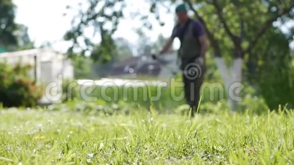在阳光明媚的夏天用汽油割草机修剪汽车割草机的模糊男工在草地上割草视频的预览图
