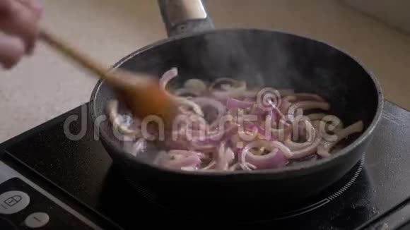 女人把洋葱放在平底锅里煎然后用木勺把洋葱混合起来特写视频的预览图