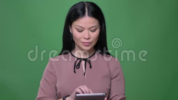 用平板电脑拍摄有着黑色头发的年轻亚洲女性的特写镜头并用蓝色的彩色屏幕显示视频的预览图