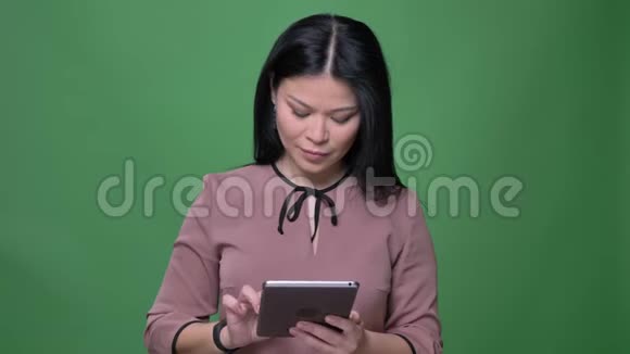 年轻迷人的亚洲女性特写镜头黑发在平板电脑上发短信背景是绿色的视频的预览图