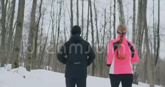 在阳光明媚的冬天早晨一对年轻健康的年轻夫妇带着运动在森林里奔跑视图视频的预览图