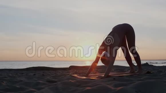 日落时练习瑜伽的年轻女子适合女孩在阳光明媚的晚上在沙滩上做弹性运动视频的预览图