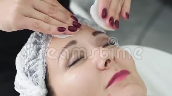 特写美容师在面部护理前用湿棉垫清洁女性皮肤视频的预览图