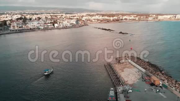 空中无人机拍摄的白色小船帆从美丽的城市港口进入开阔的海洋日落时施工视频的预览图
