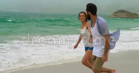白种人夫妇手牵手在海滩上奔跑的侧面景色视频的预览图