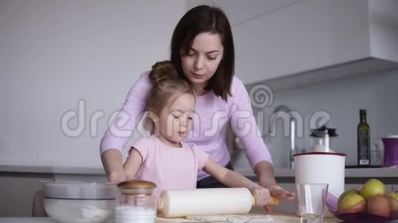 白人年轻慈爱的母亲快乐地帮助她可爱的小女儿用擀面杖擀面视频的预览图