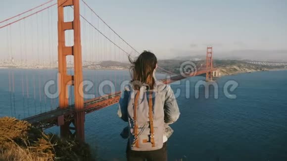 镜头接近年轻女游客背包飞毛在金门大桥美国欣赏风景日落视频的预览图