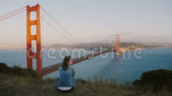 后景年轻的当地妇女独自坐在史诗般的风景冥想美丽的日落景观金门大桥美国视频的预览图
