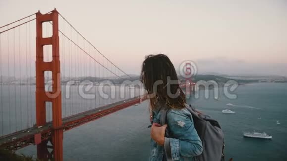 年轻女创意工携背包散步看史诗般的风景名落日金门桥在大风中视频的预览图