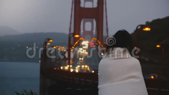 后景年轻的当地妇女独自站在黑暗的金门大桥交通景观在美国覆盖着温暖的白色毯子视频的预览图