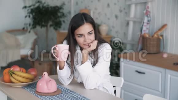 穿着浴袍的女孩的肖像享受厨房的清晨时光喝茶慢动作视频的预览图