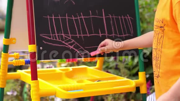 一个男孩在户外用粉笔在黑板上画画他的手特写视频的预览图
