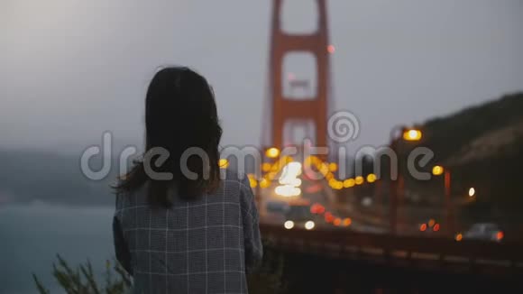后景年轻放松的女人看标志性的金门大桥在黑暗的夜晚大风的交通景观视频的预览图