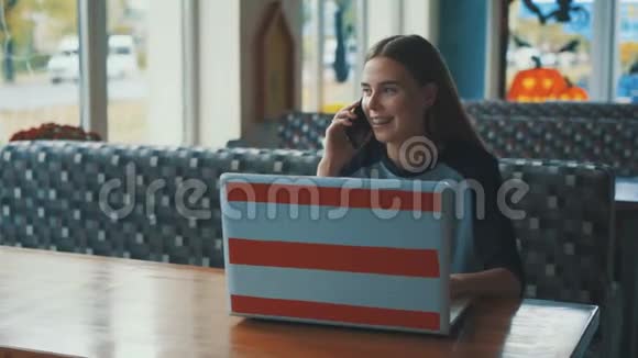年轻漂亮的女孩在咖啡馆里喝着咖啡微笑着用电脑在电话里说话视频的预览图